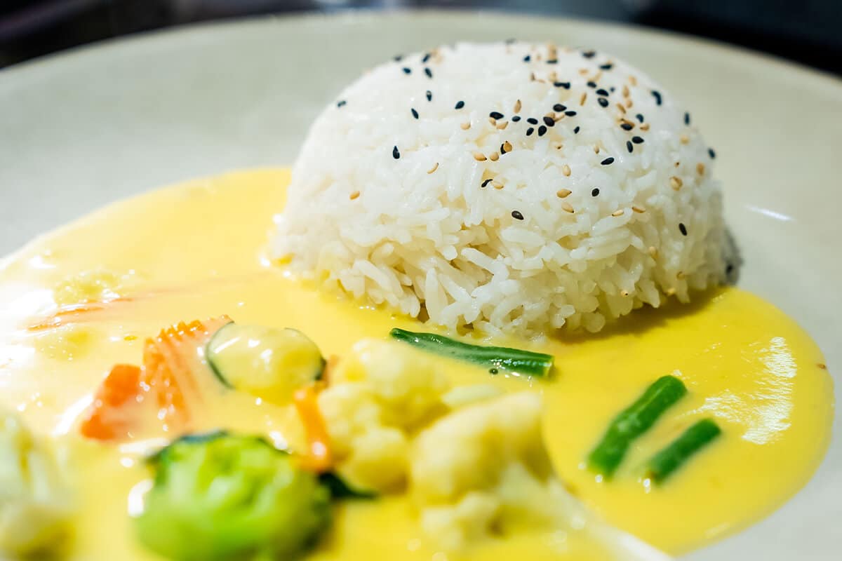 Halbkugelförmiger Reis mit schwarzen und weißen Sesamsamen, umgeben von gelber Sauce mit Gemüse