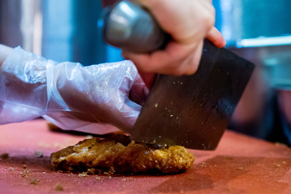 Hand mit Plastikschutzschuh hält ein Messer und zerkleinerz frittiertes Fleisch