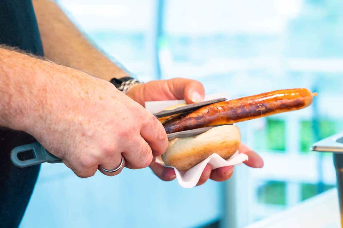 Bratwurst wird mit einer Grillzange in ein Brötchen gelegt