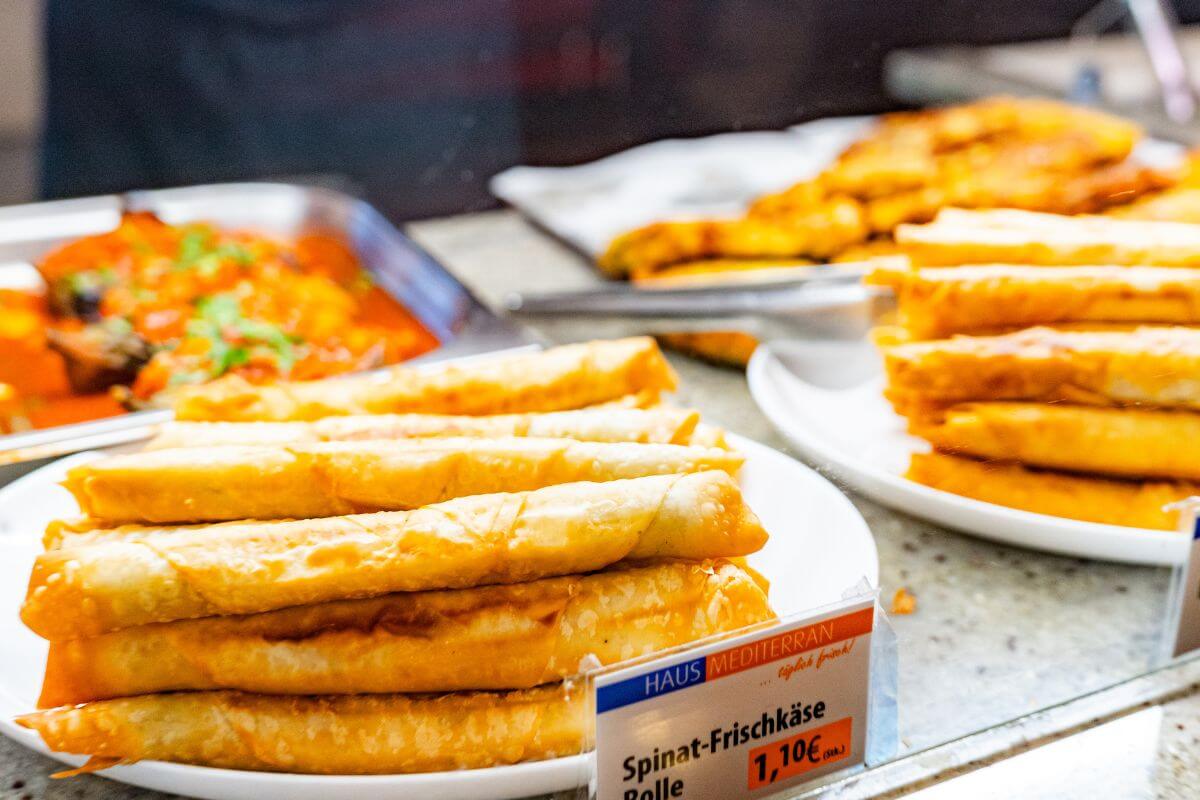 Teller mit goldbraun gebackenen Spinat-Frischkäse-Rollen in einer Auslage