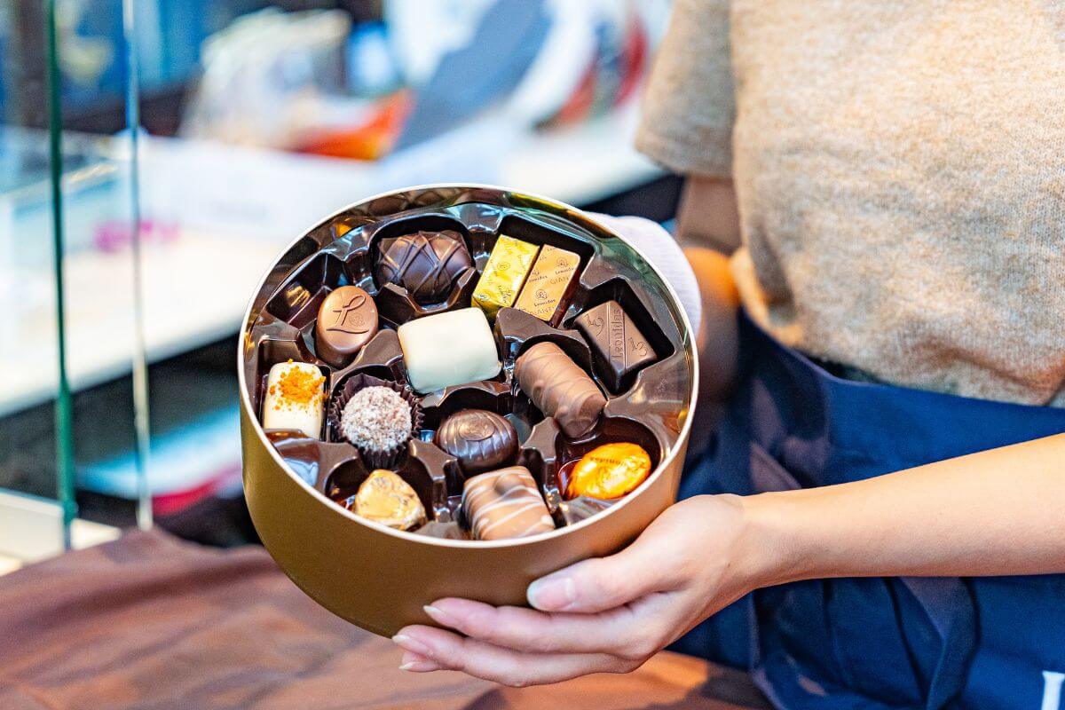 Eine Person hält eine runde Pralinenschachtel in den Händen, gefüllt mit verschiedenen belgischen Pralinen