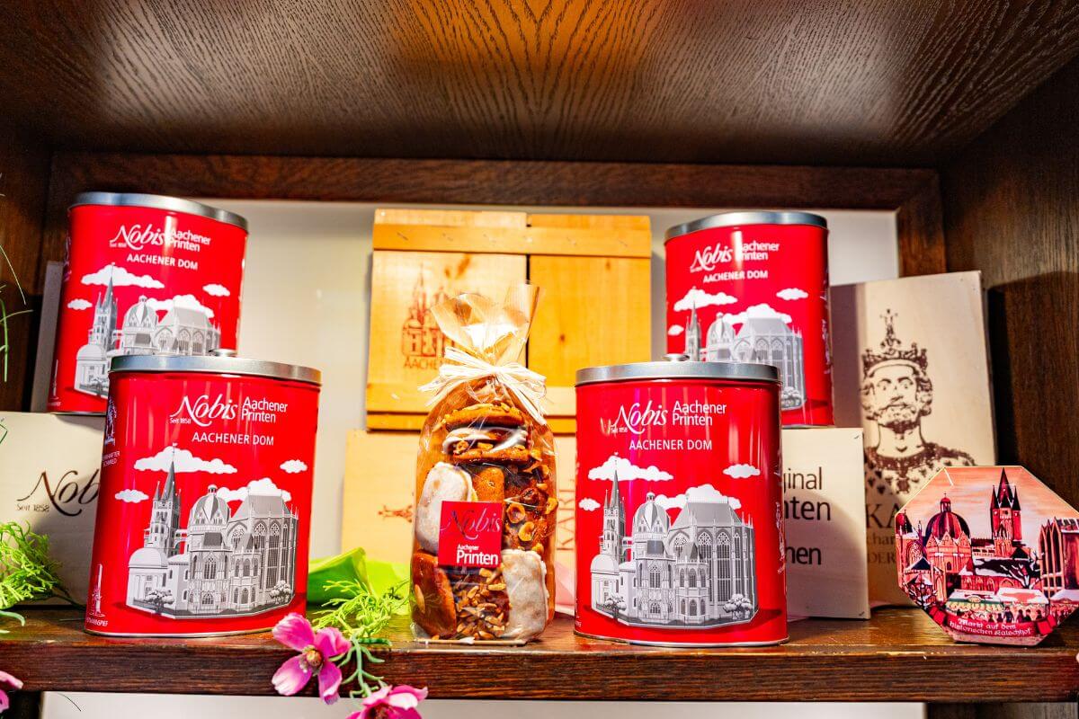 Regal mit mehreren rot-silbernen Blechdosen und mit Motiv des Aachener Doms